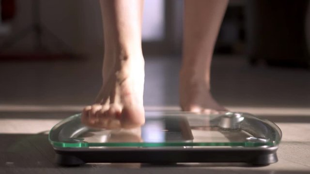 Woman measuring her weight using scales on wooden floor. Healthy diet.