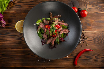 Thai beef salad in black plate on wooden background