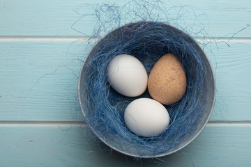 Three eggs in a dish with sisal on a blue wooden surface.