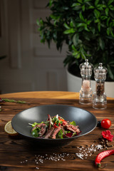 Thai beef salad in black plate on wooden background