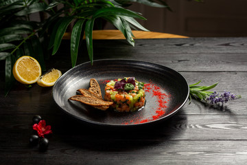 salmon tar-tar on a black plate on a wooden background