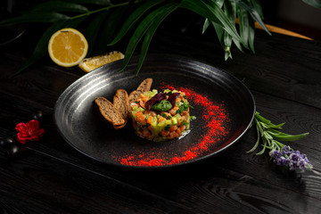 salmon tar-tar on a black plate on a wooden background