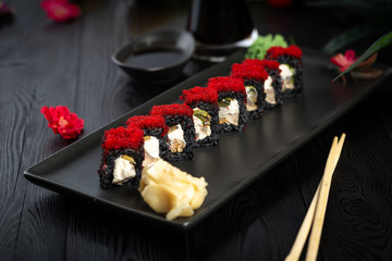 set of black sushi rolls on a black rectangular plate on a black wooden background