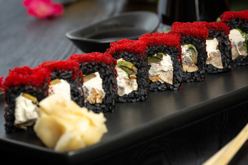 set of black sushi rolls on a black rectangular plate on a black wooden background