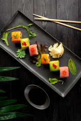 set of sushi rolls on a black rectangular plate on a black wooden background
