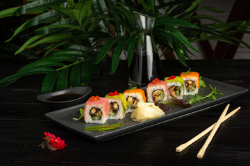 set of sushi rolls on a black rectangular plate on a black wooden background