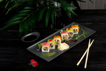 set of sushi rolls on a black rectangular plate on a black wooden background