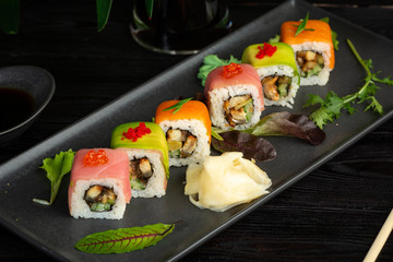 set of sushi rolls on a black rectangular plate on a black wooden background