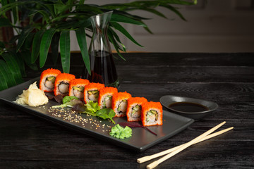 set of sushi rolls on a black rectangular plate on a black wooden background