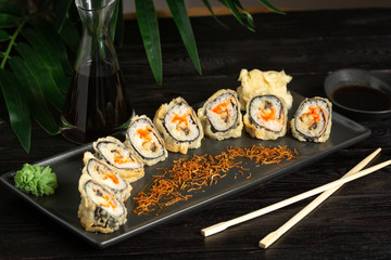 set of sushi rolls on a black rectangular plate on a black wooden background