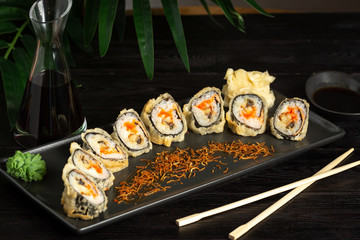 set of sushi rolls on a black rectangular plate on a black wooden background