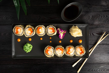 set of sushi rolls on a black rectangular plate on a black wooden background