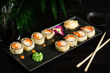 set of sushi rolls on a black rectangular plate on a black wooden background