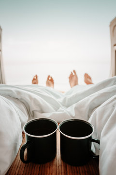 Zwei Kaffeetassen am Bett eines VAN mit Blick auf das Meerund im Hintergund F&uuml;sse 