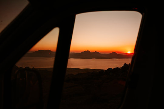 Blick aus einem Camper Van bei Sonnenuntergang auf einen Stausee und im Hintergrand das Atlasgebirke in Marokko