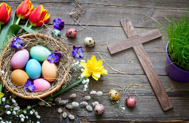 Easter colorful eggs in the nest with flowers on vintage wooden boards with cross