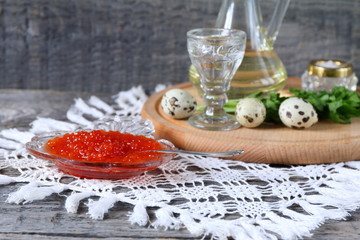 Red caviar in glassware near the glass of vodka on a gray wooden background.