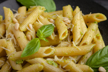 Penne pasta on black plate and black table with pesto sauce parmesan and basil. Italian food. Copyspace for your text.