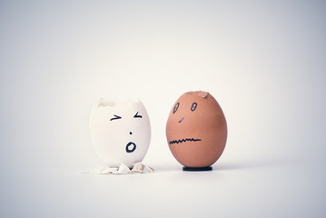 Two broken eggs in the form of human head (white and black)  complain to each other. Concept.