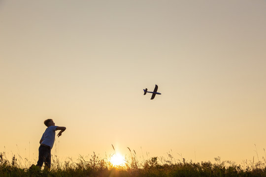 Young happy kid playing toy plane outside on summer sunset grassy hill. Horizontal color photography.
