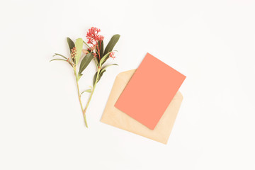 Minimal composition with a paper envelope, coral blank card and flower on a white background. Mockup with envelope and blank card. Flat lay. Top view