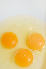 Three broken chicken eggs in a white mixing bowl