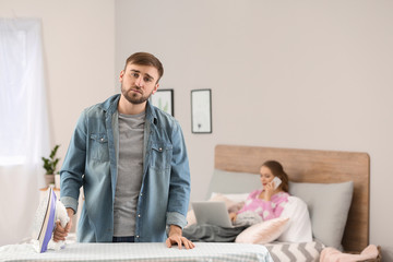 Obraz premium Househusband ironing clothes while his wife working in bed