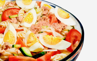 Traditional tuna salad. Tuna, pasta, eggs and vegetables in a glass dish on a white background. Selective focus.