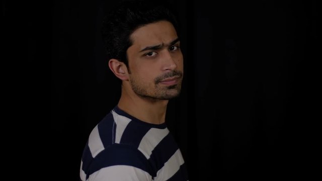 Young confident Indian man turns his neck sideways and looks directly to the camera with a disapproval and unsatisfied  and nods his head in disagreement and then back 