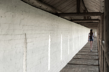 The girl walks along the long aisle of the monastery against the background of a white wall.