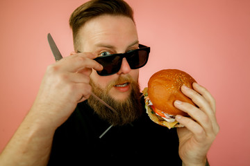 stylish guy eating a Burger, young guy holding a Burger in his hands, man eating fast food on a pink background,
