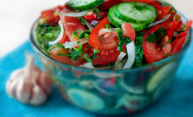 Salad with tomato, cucumber, onion, pepper, dill, parsley, olive oil, spice. Head of garlic. Selective focus. Blurred background.