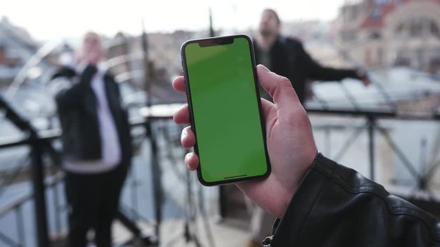 Close up selective focus on male hand using smartphone with green display in vertical position, taking photos of friends. Tapping the screen, flagman, modern technologies. Advertisement concept.