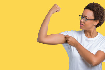 Beautiful young african american woman wearing glasses over isolated background showing arms muscles smiling proud. Fitness concept.