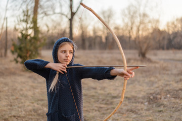 A girl with a homemade bow in her hands in the rays of sunset on nature.