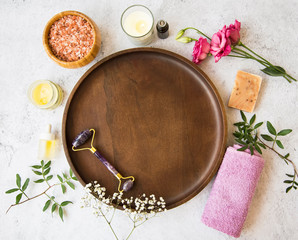 Fototapeta na wymiar Top view of spa setting with wooden plate, skincare and beuty products, amethyst face roller, flowers, towel oil bottle, bath salt , candle, plants essential oil, natural spa still life