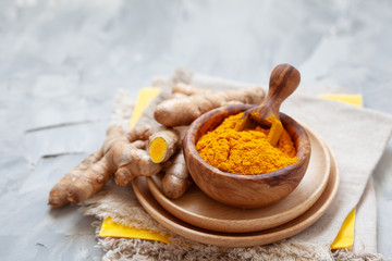 Turmeric powder in wooden bowl and fresh turmeric on light grey backgound close-up