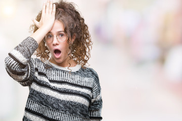 Beautiful brunette curly hair young girl wearing glasses over isolated background surprised with...
