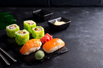 Various Fresh and delicious sushi set on black slate with slate sticks, sauce and nori on black stone background , flat lay