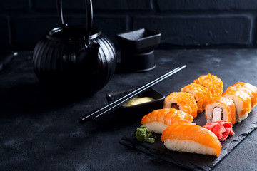 Asian food background with black iron teapot and sushi set on slate plate on black stone table