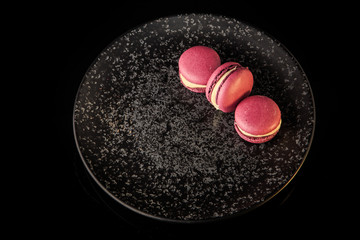 top view three purple macaroons served on black plate