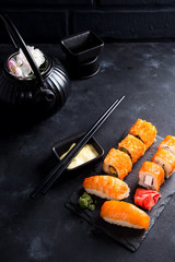 Asian food background with black iron teapot and sushi set on slate plate on black stone table