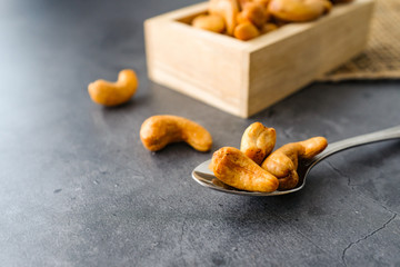 Dried roasted cashew nuts in natural wooden box container in stainless steel metal spoon and sackcloth on dark grey concrete table top with copy space. Healthy and organic food lifestyle concept.