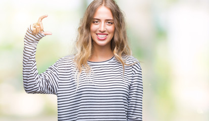 Beautiful young blonde woman wearing stripes sweater over isolated background smiling and confident gesturing with hand doing size sign with fingers while looking and the camera. Measure concept.