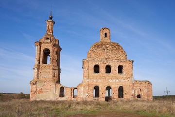 Old destroyed and abandoned church against the blue sky, in the middle of the field