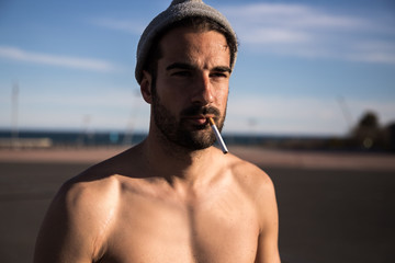 man without t shirt wearing a beanie being outdoors with a cigarette in his mouth © marc