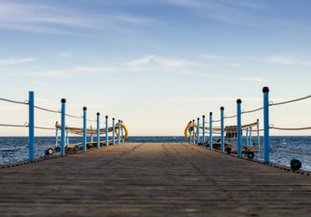 Obraz premium wooden platform with blue posts with ropes and orange lifebuoys on the background of the sea and sky with clouds Egypt Dahab South Sinai