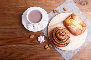 a cup of hot chocolate and buns  on brown wooden background.