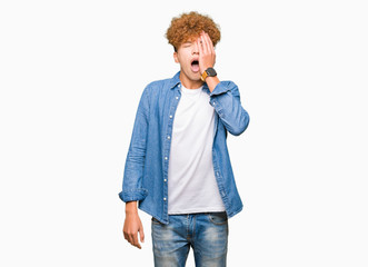Young handsome man with afro hair wearing denim jacket Yawning tired covering half face, eye and...