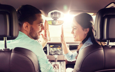leisure, road trip, travel and people concept - happy man and woman driving in car and looking back